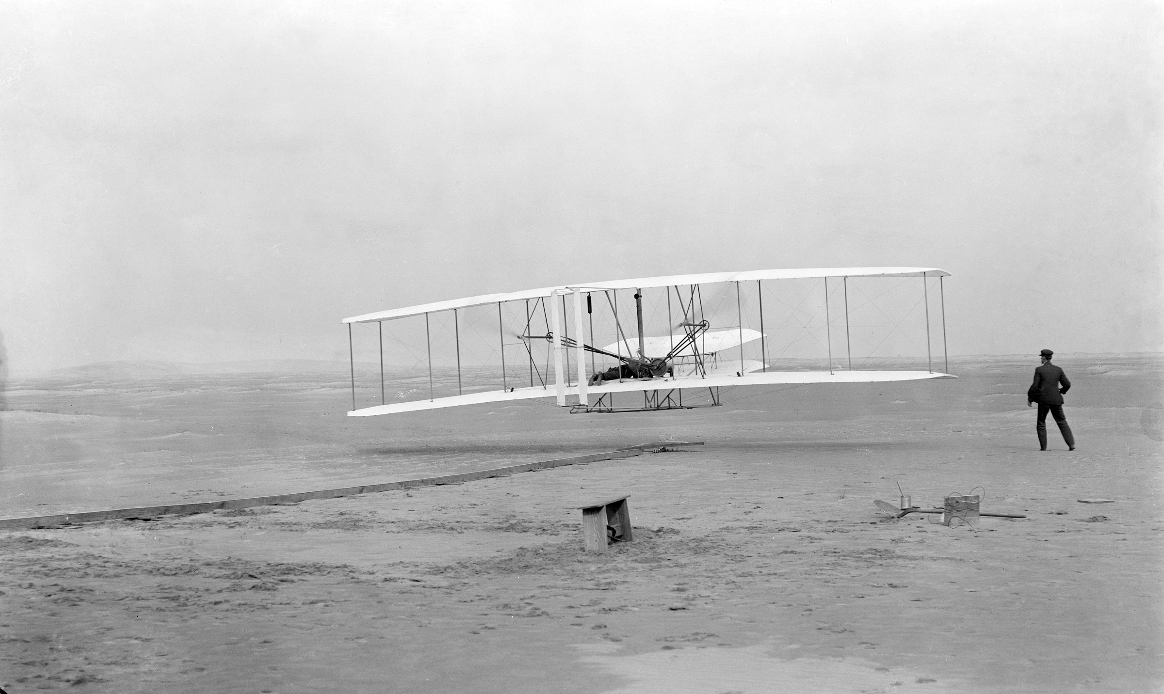The first flight of the Wright Flyer at Kill Devil Hills, 17 December 1903: the biplane a few feet above the sand, Wilbur Wright running alongside.