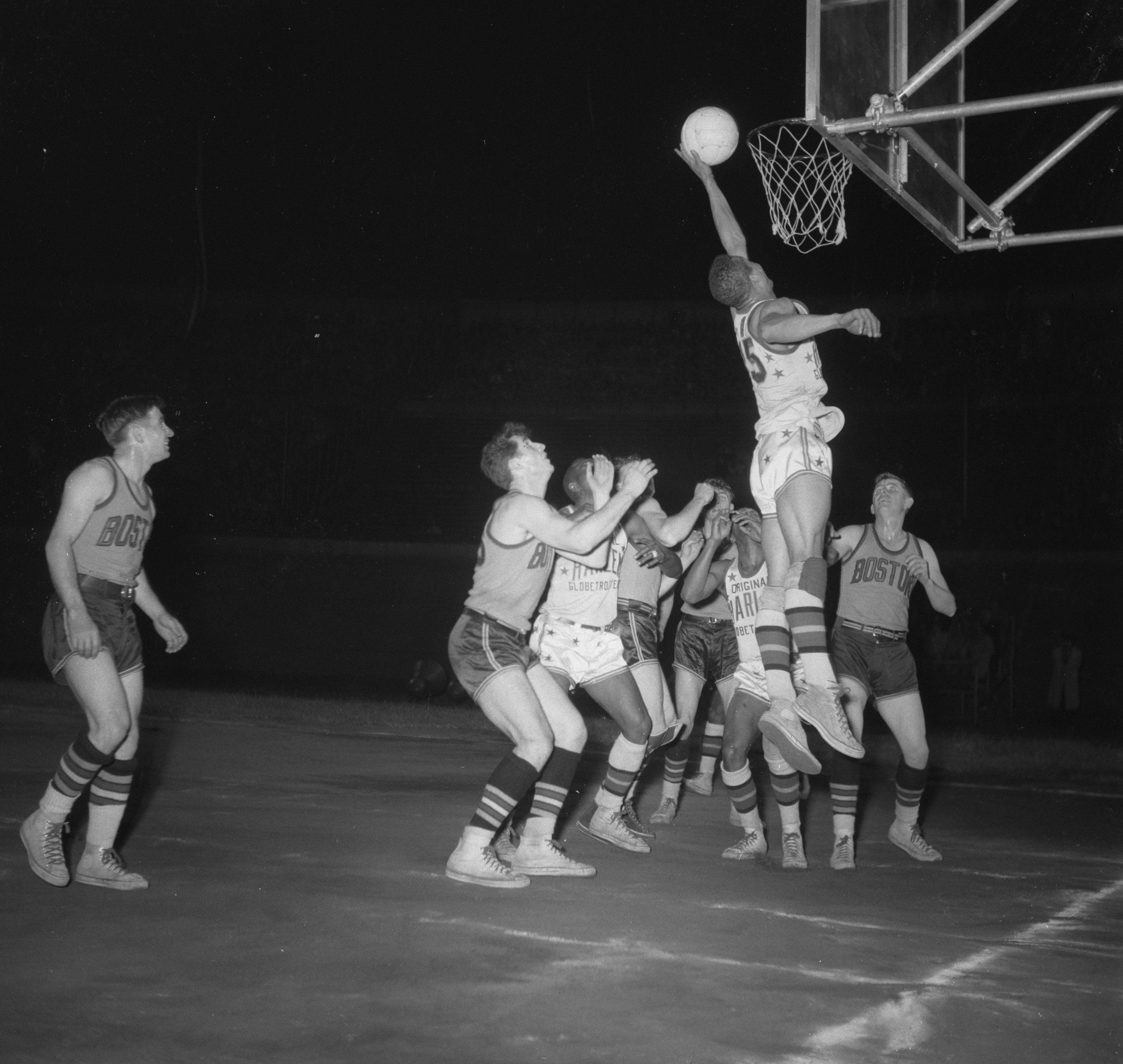 A black-and-white photograph of the Harlem Globetrotters in Amsterdam, 1951: a player leaps at the basket with the ball on the rim.