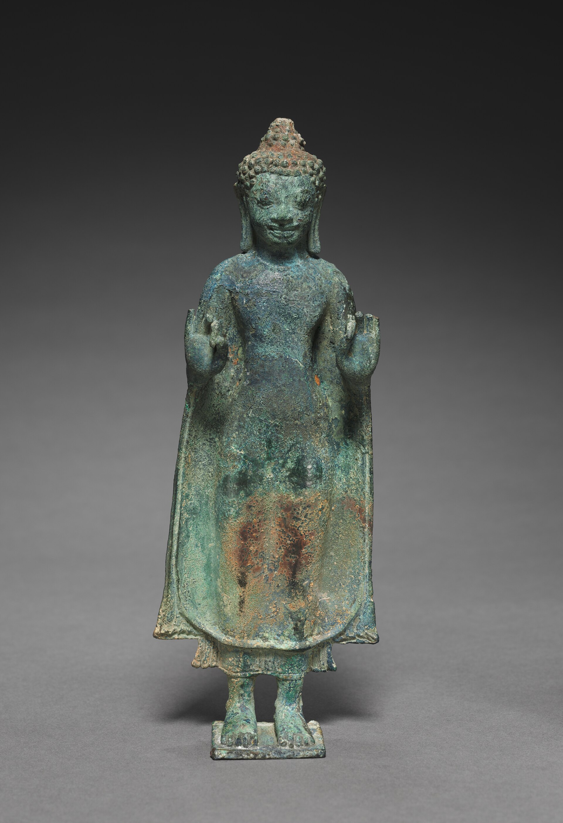 A seventh-century stone Buddha from Thailand with both hands raised in the vitarka mudra, the gesture of teaching.
